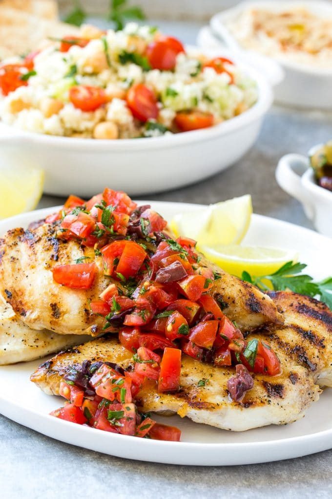 A plate of grilled Greek lemon chicken topped with tomatoes and olives.