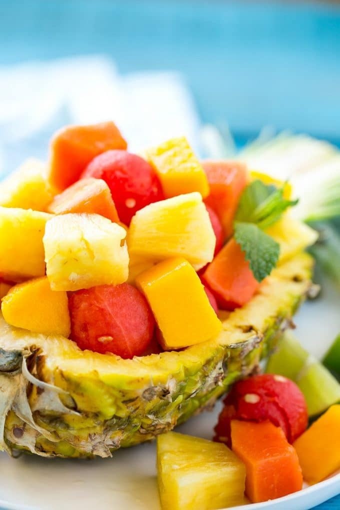 A pineapple half filled with melon, papaya and mango.