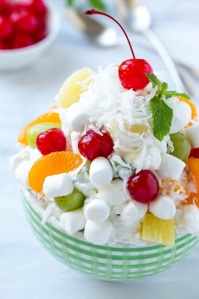 A bowl of ambrosia salad topped with coconut, marshmallows, fruit and a cherry.