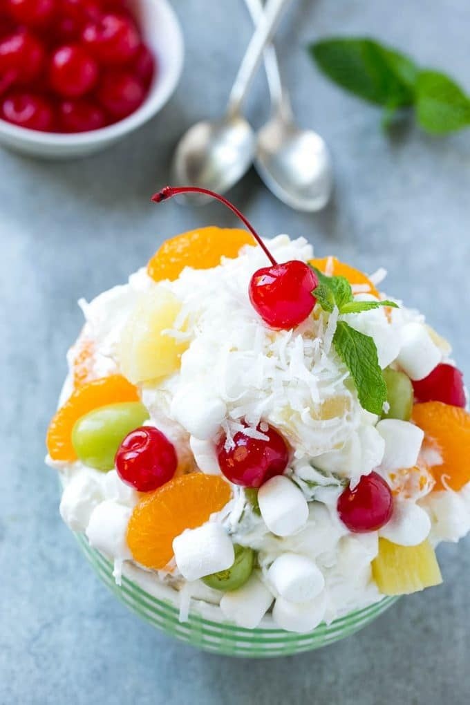 A bowl of ambrosia salad topped with coconut and a cherry.