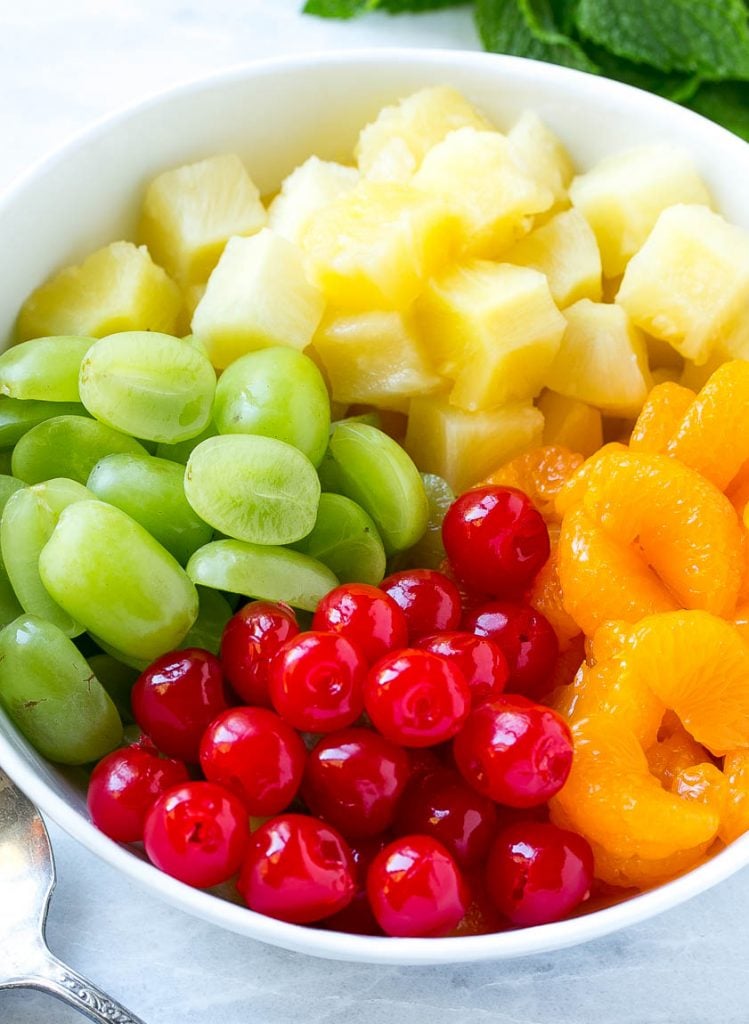 A bowl of oranges, pineapple, grapes and cherries.