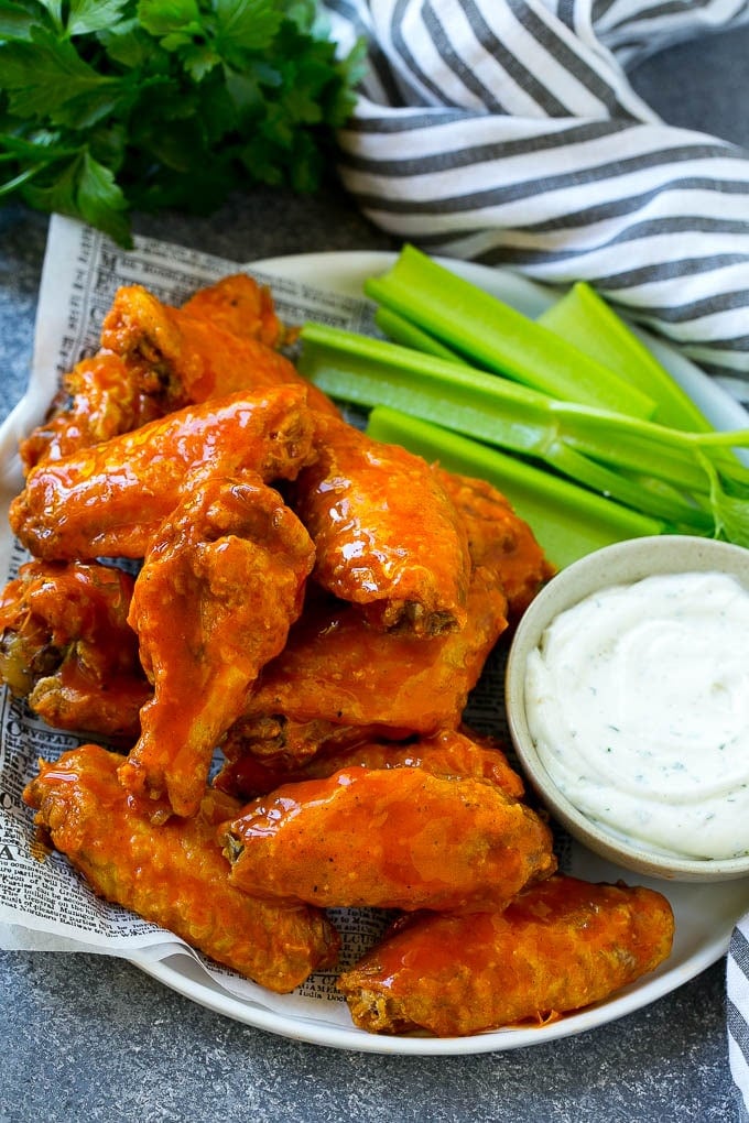 A pile of baked buffalo wings with celery sticks and ranch dressing.