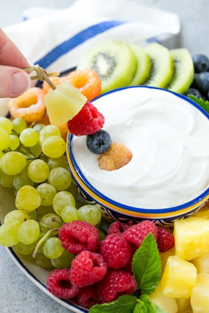 A skewer of berries going into a bowl of fruit dip.