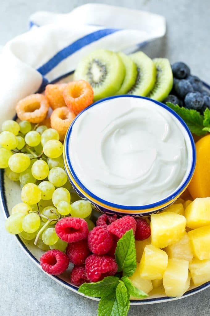 A bowl of cream cheese fruit dip surrounded by colorful fruit.