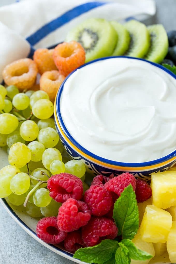 A bowl of cream cheese fruit dip surrounded by grapes, raspberries and kiwis.