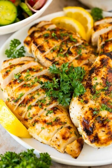 Sliced grilled Greek lemon chicken with lemon wedges and parsley.