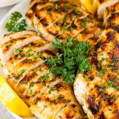 Sliced grilled Greek lemon chicken with lemon wedges and parsley.