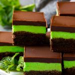 Layered mint brownies with frosting on a serving plate, garnished with fresh mint.