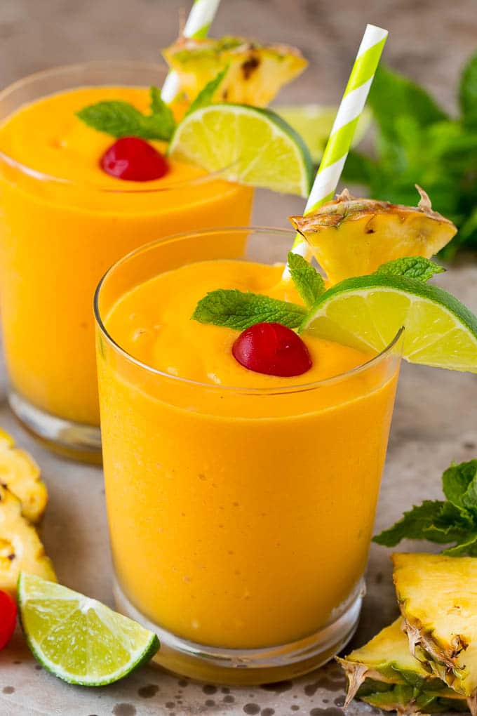 Mango pineapple smoothies garnished with cherries and mint.