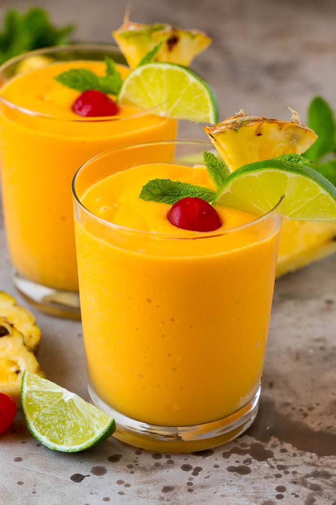 Two tropical smoothies with fresh mint, lime wedges and sliced pineapple.