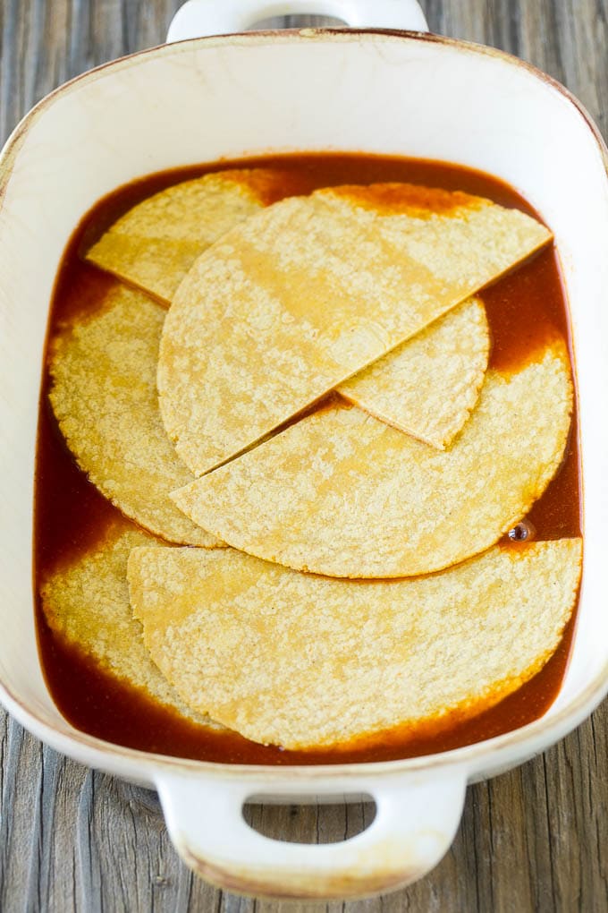 Corn tortillas and enchilada sauce in a casserole dish.