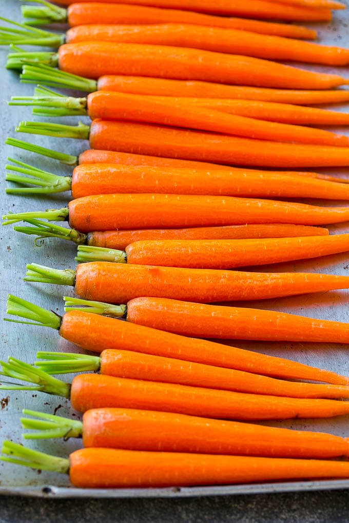 A row of peeled baby carrots on a baking pan.