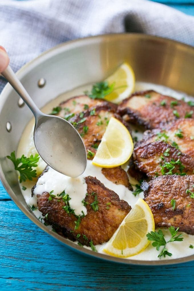 Pork scallopini in a pan with a spoon drizzling creamy sauce over the top.