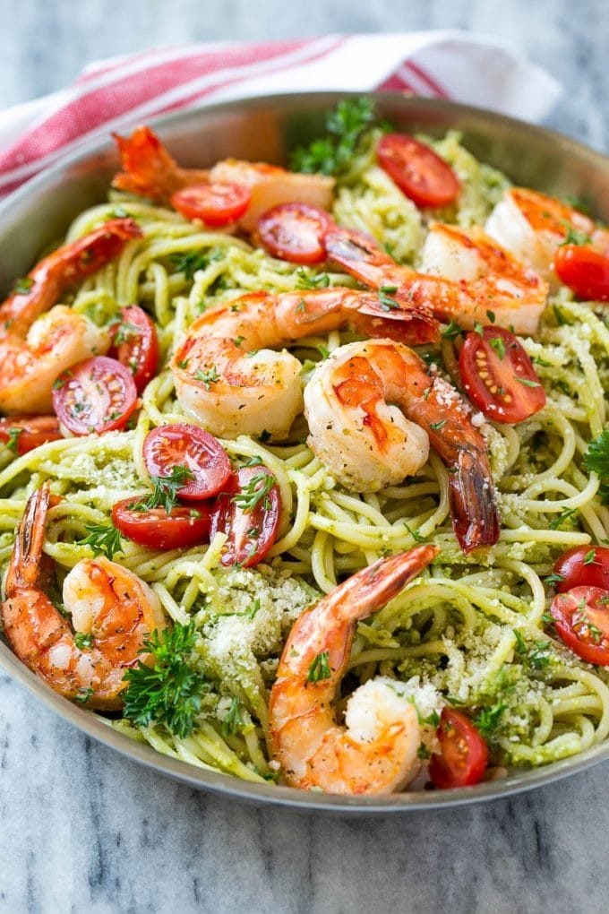 A pan of shrimp pesto pasta topped with tomatoes, parmesan cheese and parsley.