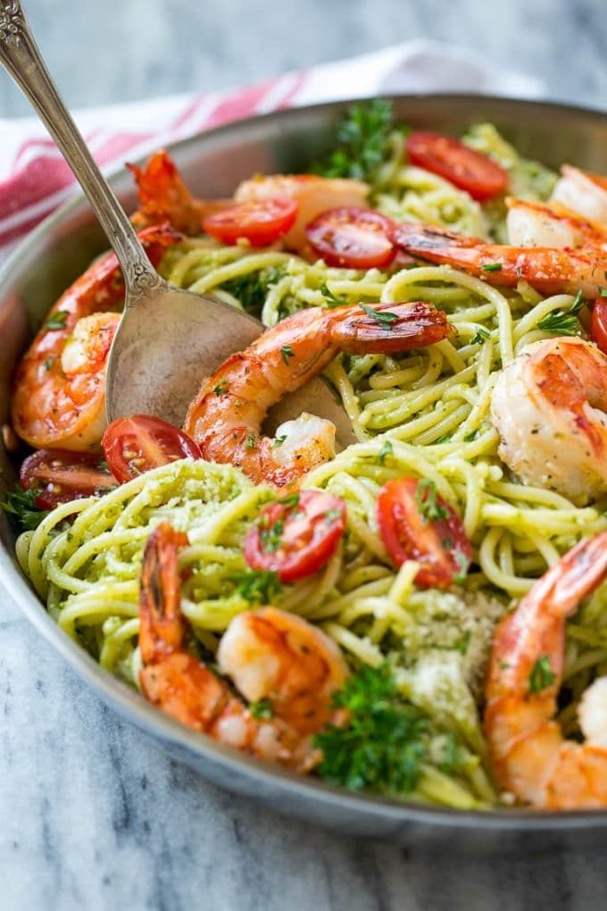 A serving spoon with a cooked shrimp in a pan of pesto pasta.