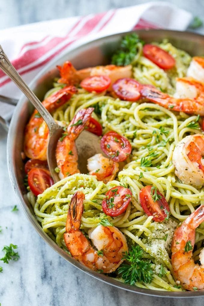 A serving spoon in a pan of shrimp pesto pasta.