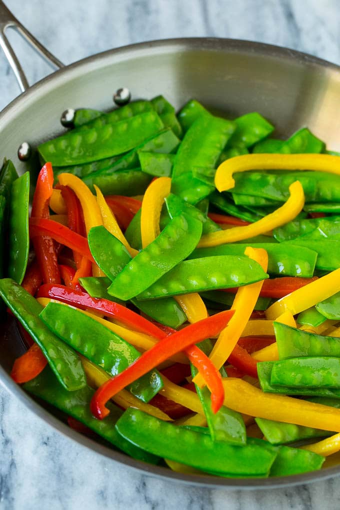 Cooked snow peas and bell peppers in a skillet.