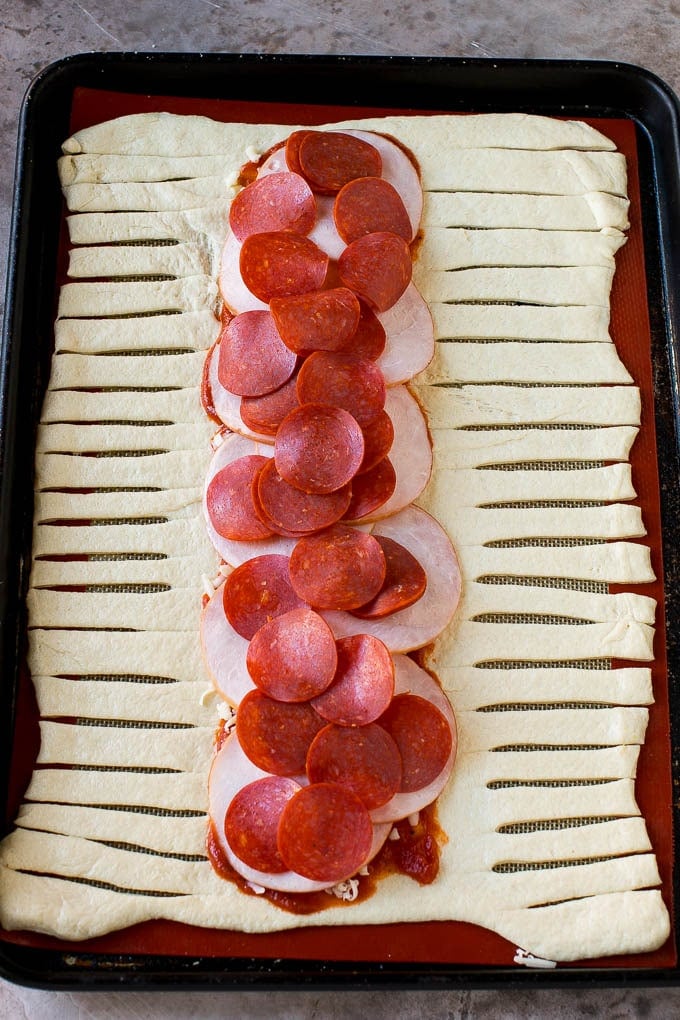 A sheet of pizza dough topped with tomato sauce, mozzarella cheese, pepperoni and Canadian bacon.