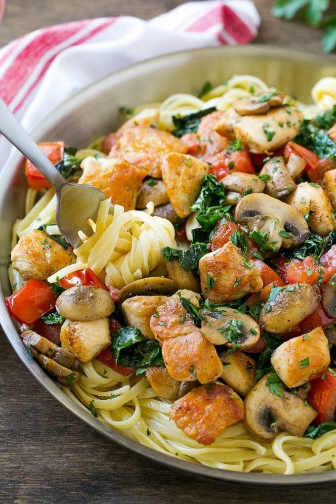 A fork serving a portion of Tuscan chicken pasta with mushrooms, tomato and kale.