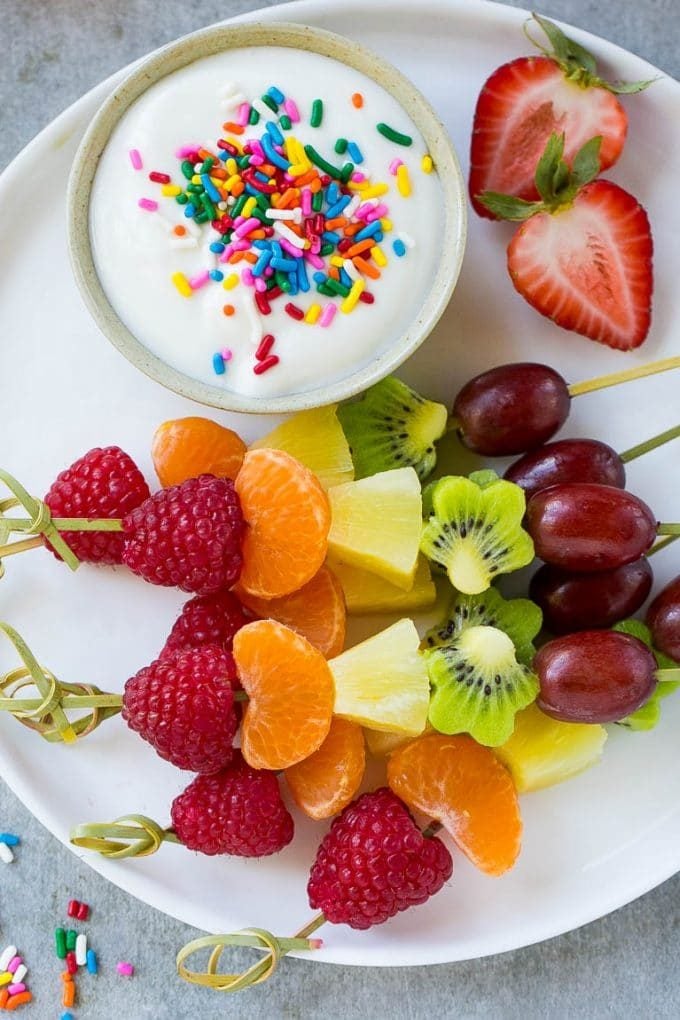Rainbow fruit skewers on a serving plate with a yogurt sauce.