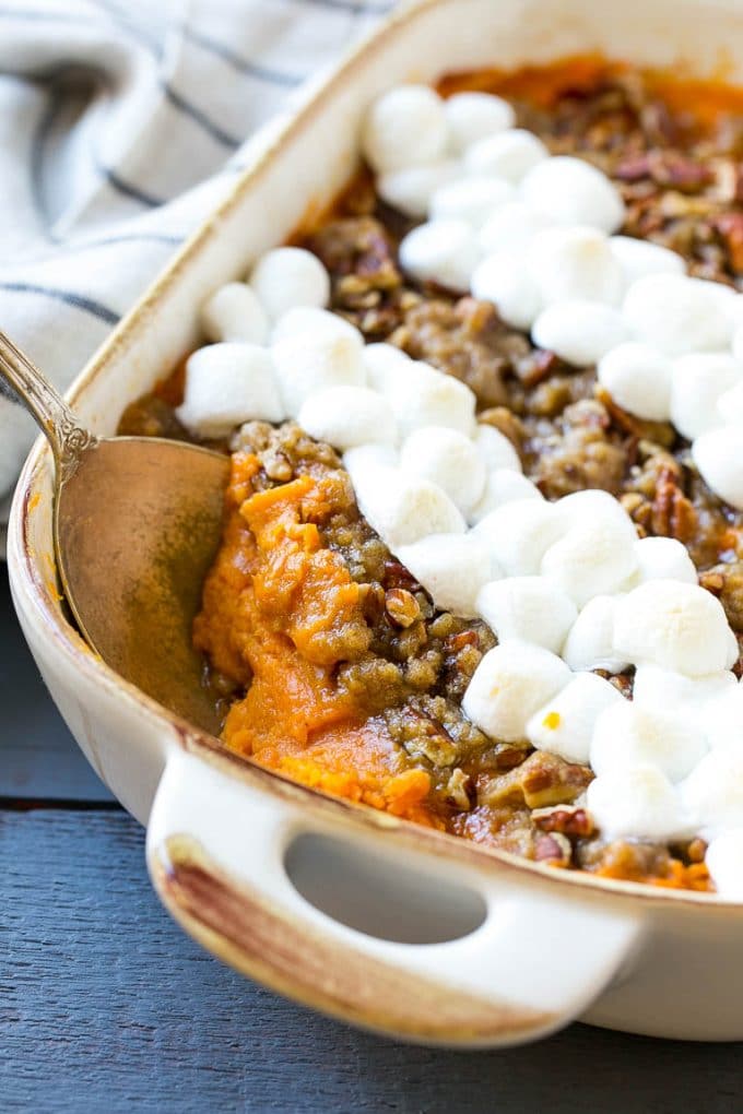 Sweet Potato Casserole with Marshmallows in a white baking dish with a serving spoon in it.