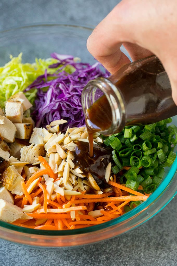 Dressing being poured over cabbage, carrots, chicken and green onions.