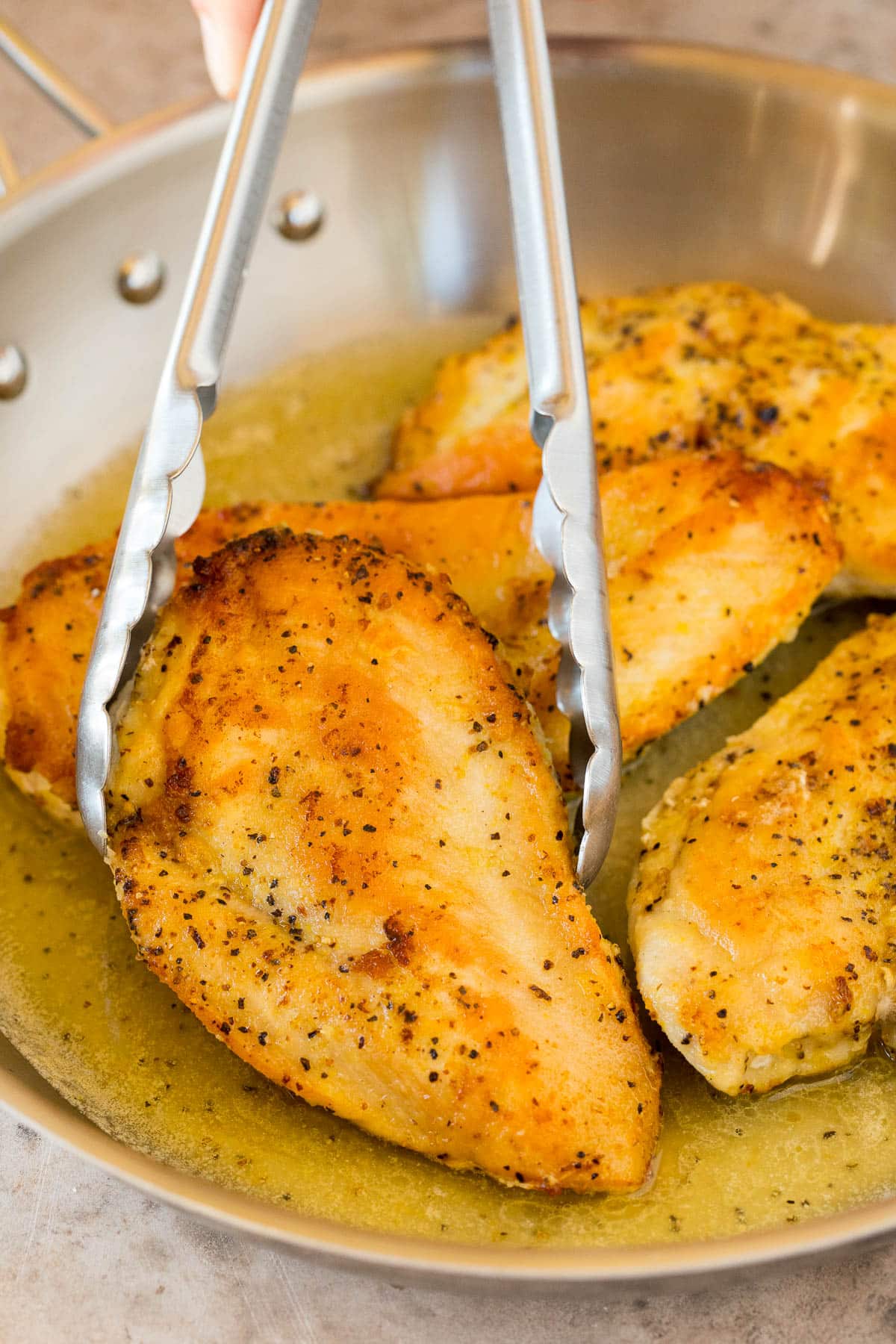 Tongs removing a chicken breast from a pan.