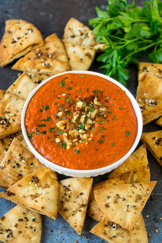 Muhammara dip in a bowl surrounded by pita chips.