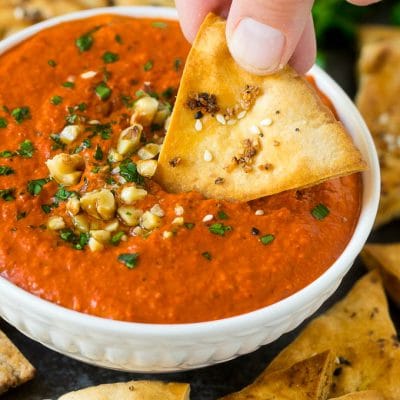 A pita chip dipping into a bowl of muhammara red pepper dip.