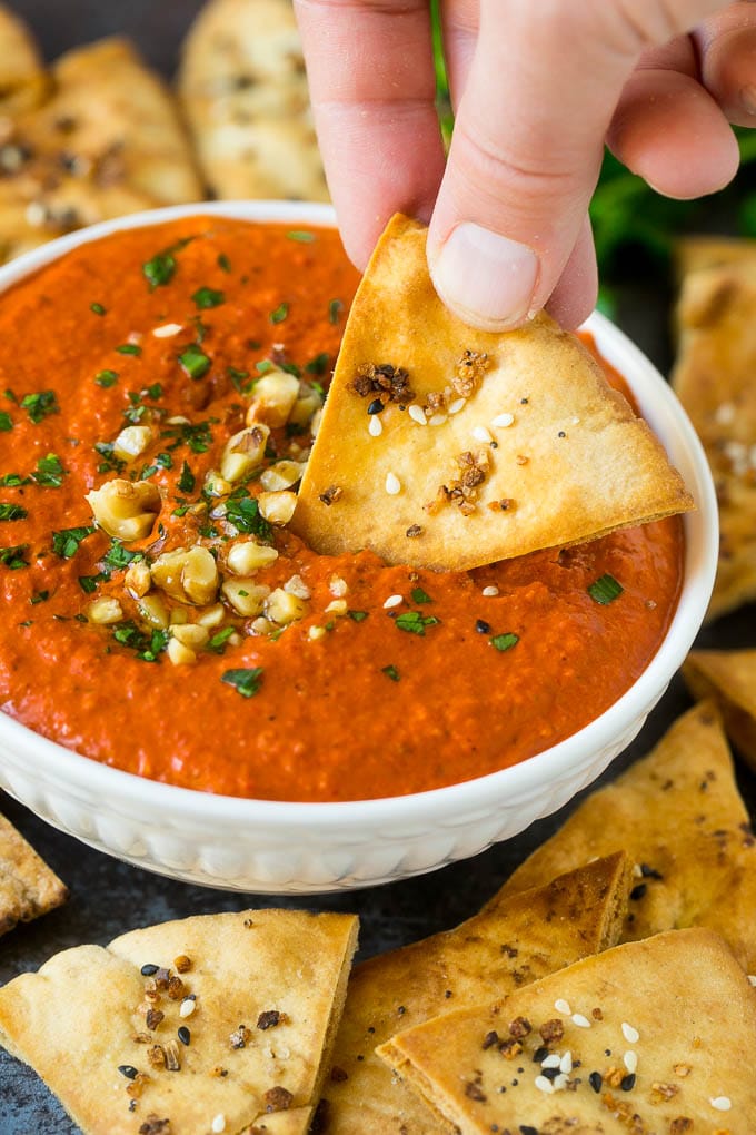 A pita chip dipping into a bowl of muhammara red pepper dip.