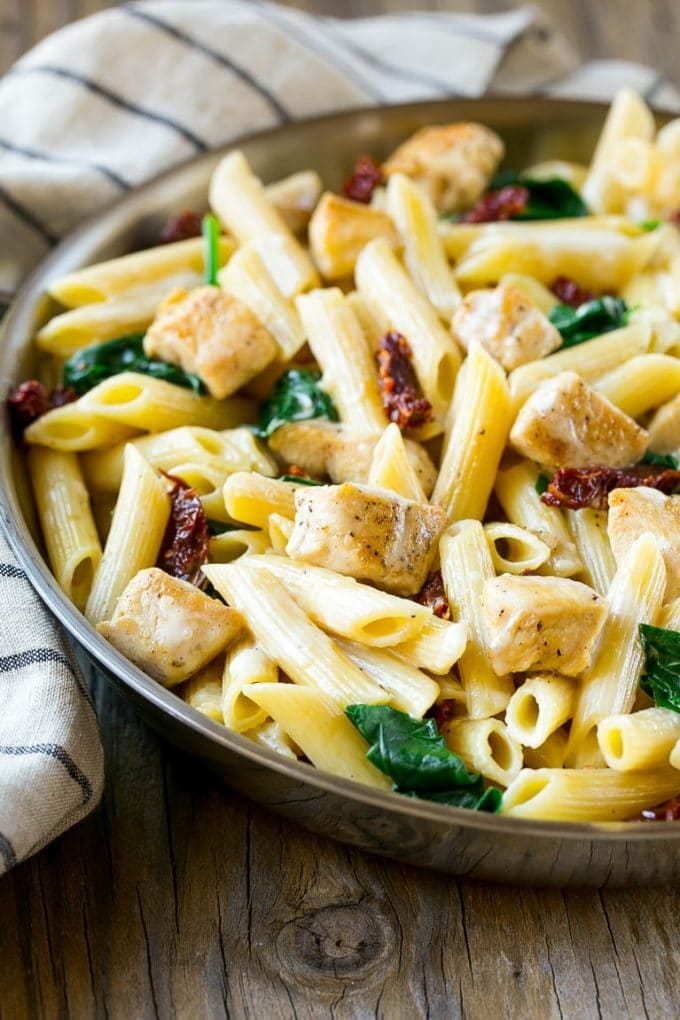 A skillet with penne pasta, sun dried tomatoes, chicken and creamy sauce.