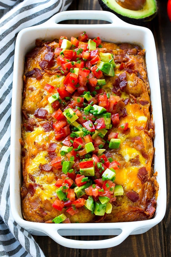 A breakfast casserole with bacon that is topped with avocado and tomato.