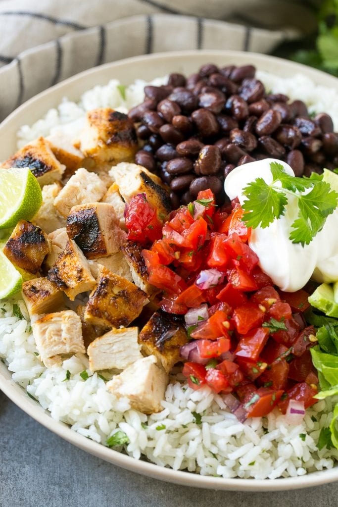 A bowl filled with cilantro lime rice, chicken, beans, sour cream and salsa.