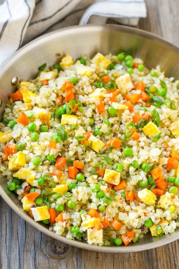 A pan full of cauliflower fried rice with carrots, eggs, peas and topped with green onions.