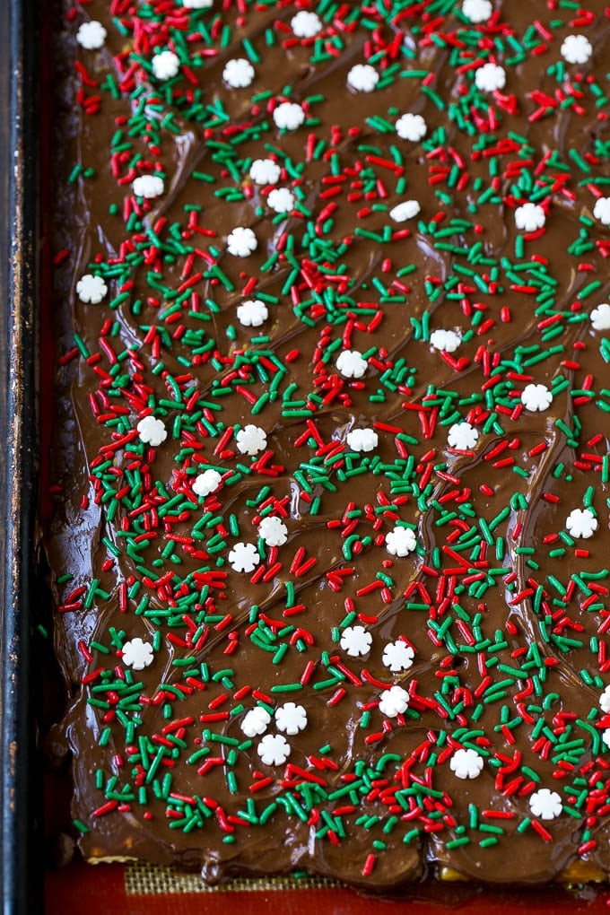 A sheet pan of Christmas crack toffee topped with melted chocolate and sprinkles.