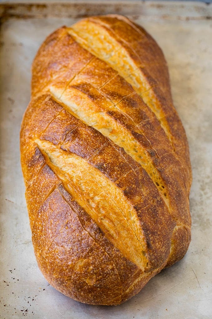 A loaf of bread on a sheet pan with diagonal cuts in it.