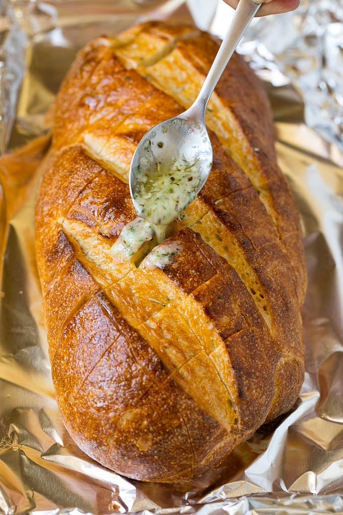 A spoon drizzling garlic butter over a loaf of bread.