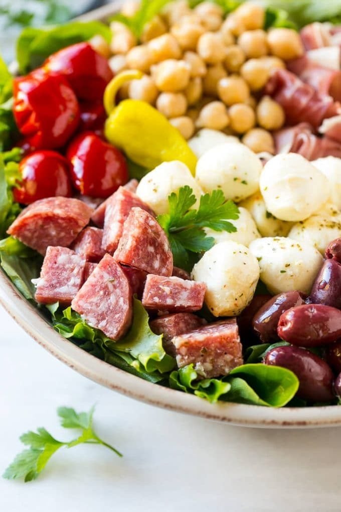 A bed of greens topped with antipasto salad including meats, cheeses, beans and vegetables.