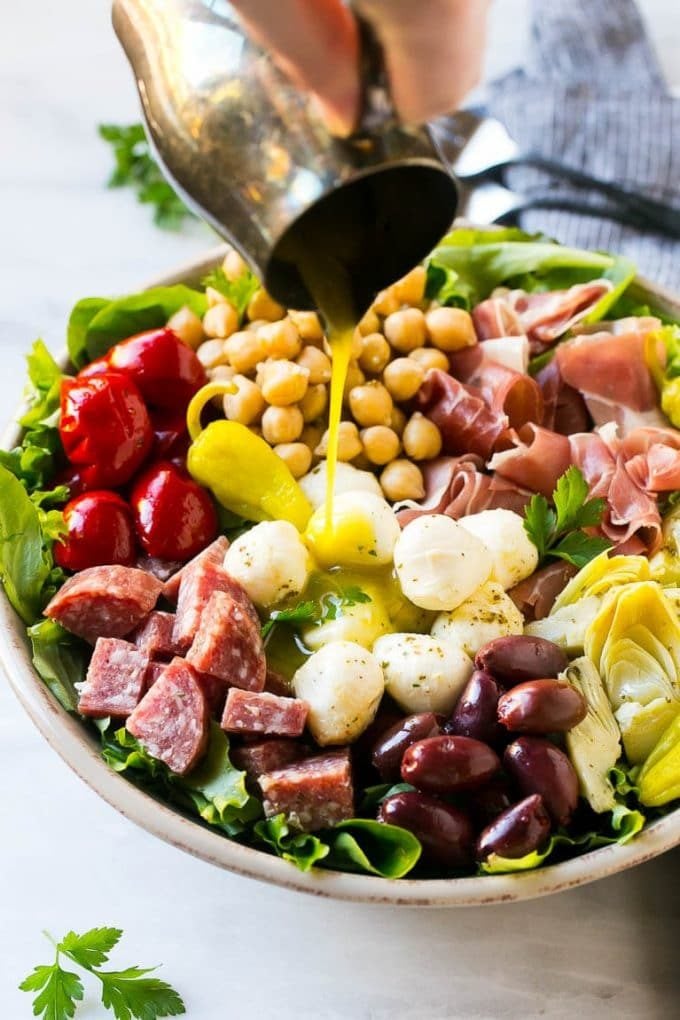 A pitcher of dressing being poured over antipasto salad.