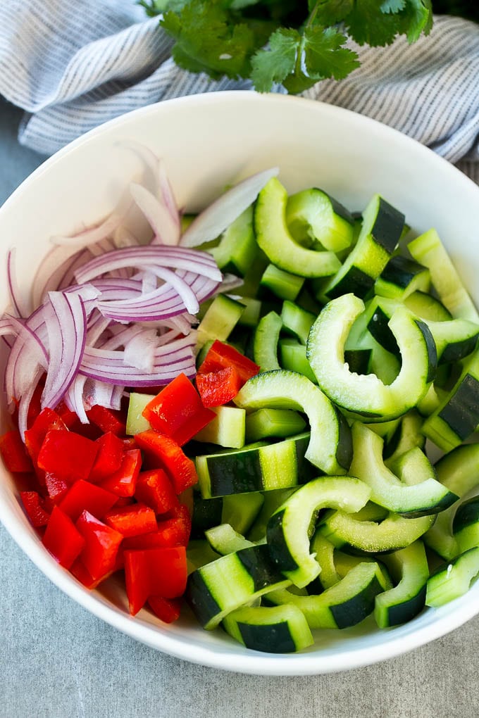 Sliced cucumbers, red peppers and red onion in a serving bowl.