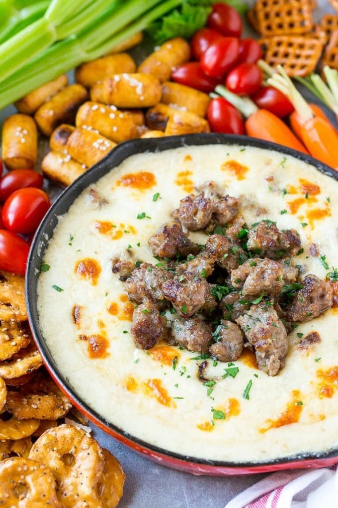 A skillet of beer cheese dip topped with bratwurst and served with vegetables and pretzels.