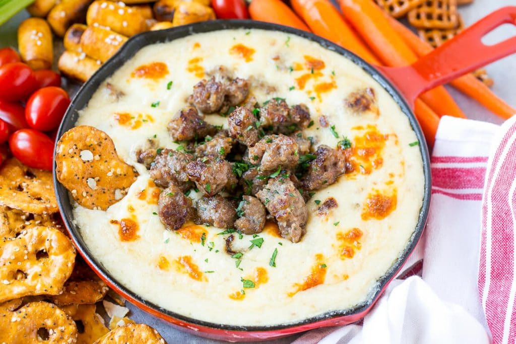 Beer cheese dip in a red skillet topped with cooked crumbled bratwurst sausage.