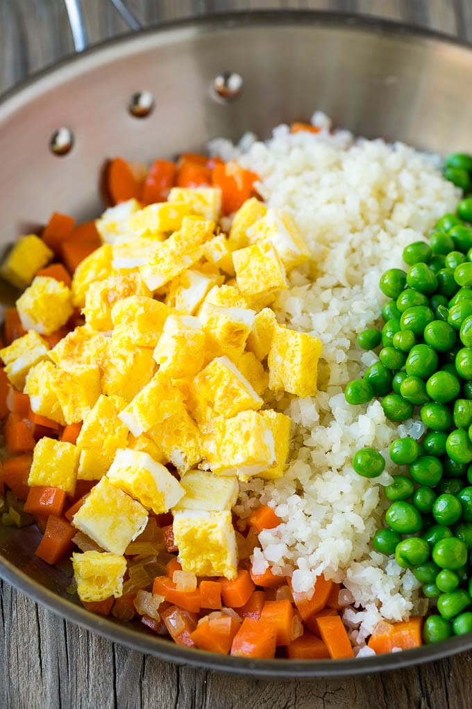 Carrots, onions, fried eggs, peas and cauliflower rice in a pan.