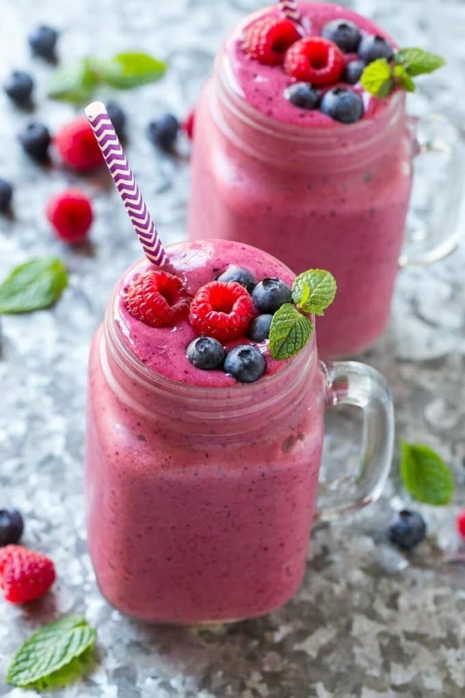 Mixed berry smoothie in a clear glass mug with raspberries and blueberries on top.