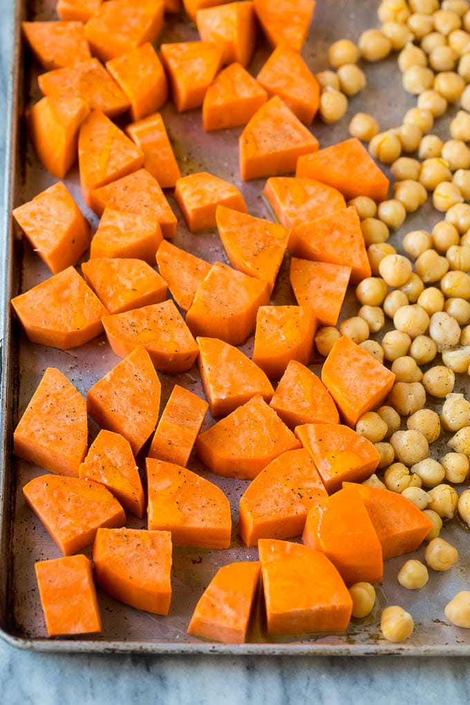 Raw sweet potatoes and canned chickpeas on a sheet pan.