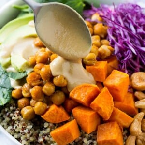 Buddha Bowl with quinoa, chickpeas, sweet potatoes, avocado, cabbage, tahini dressing poured over the top