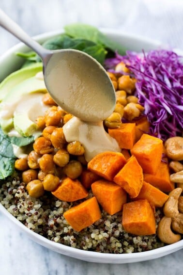 Buddha Bowl with quinoa, chickpeas, sweet potatoes, avocado, cabbage, tahini dressing poured over the top