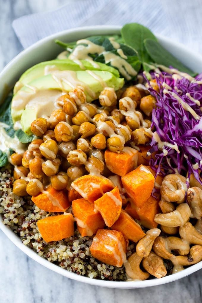 A Buddha bowl filled with quinoa, sweet potatoes, chickpeas and avocado, then drizzled with tahini dressing.