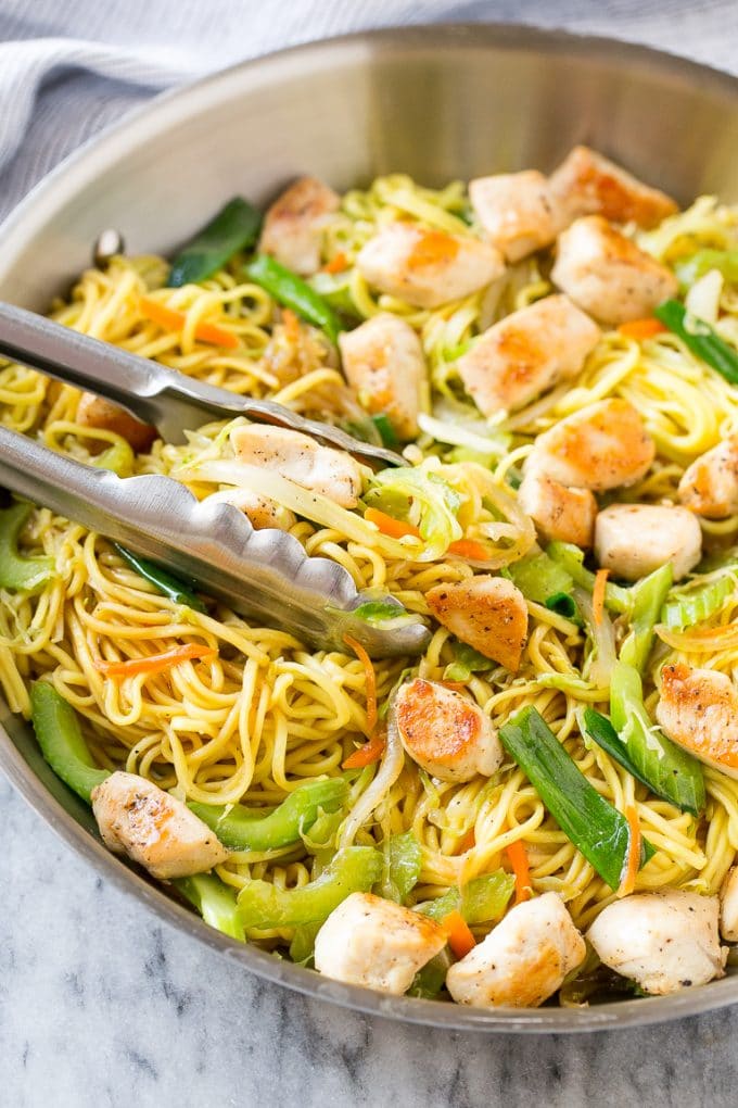 A pan of chicken chow mein with serving tongs in it.