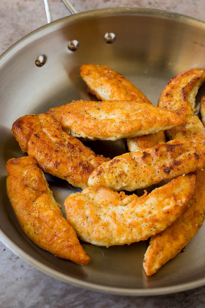 Breaded and seared chicken tenders in a skillet.